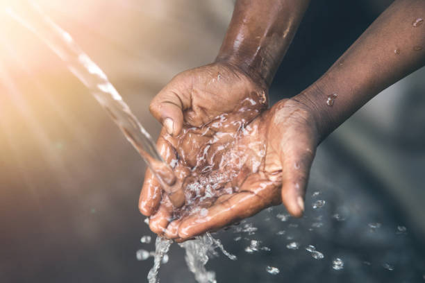 The hands of a child from a poor community are outstretched to receive a flowing stream of clear, fresh water.